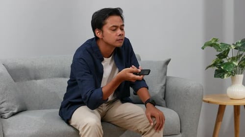 Man Sitting on Sofa Using TV Remote Control
