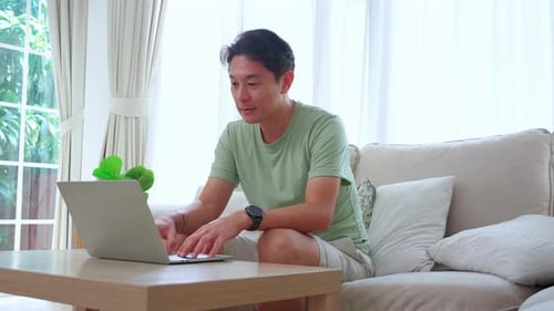 Young asian man typing keyboard on laptop computer on desk at home.