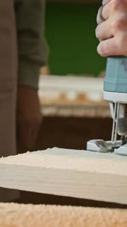 Vertical Close-Up of Carpenter Shaking Sawdust off Plank, Making Cut with Jigsaw