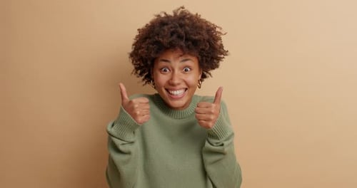 Smiling Woman Gives Thumbs Up on Beige Background