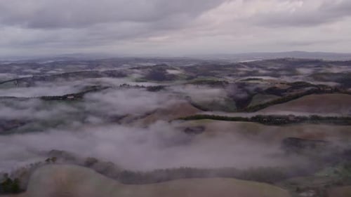 Aerial view of misty countryside with rolling hills, Italy.