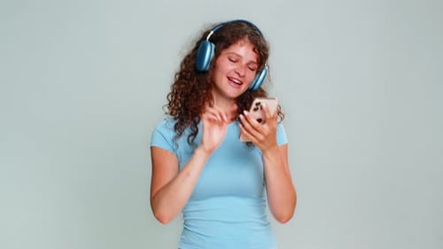 Happy young woman dances with headphones, using phone