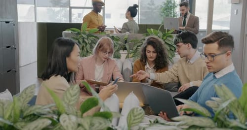 Group of Businesspeople Discussing Ideas Talking and Using Laptops in Creative Shared Office