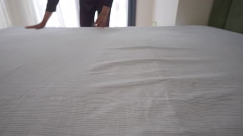 Adult Making Bed Indoors with Striped Sheets