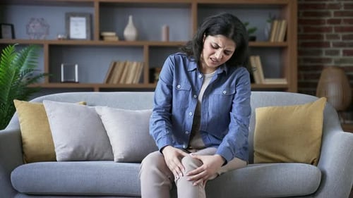 Young Woman Experiencing Knee Pain on Couch
