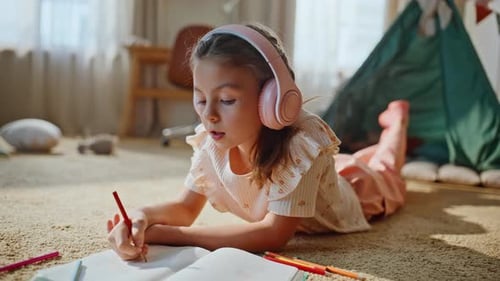 Girl Lying on Carpet Drawing and Listening Headphones