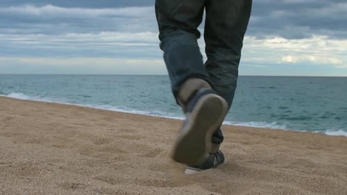 View of the legs of an adult man walking towards the sea on the beach. View of foots walking.