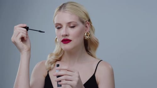 Glamorous woman applying mascara in studio setting