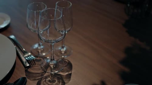 Close-up of empty wine glasses arranged on a wooden table, with plates and cutlery beside them.