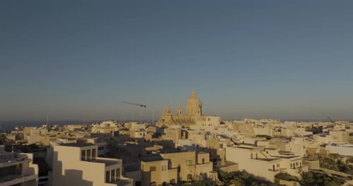 Aerial view of church and rooftops by sea at sunset, Malta.
