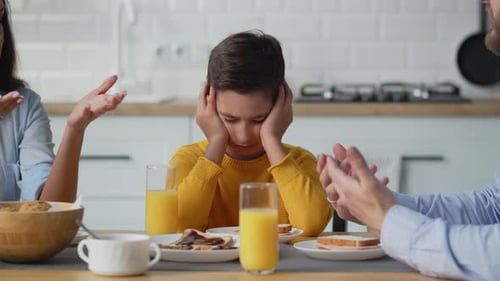 Niño molesto tapándose las orejas mientras sus padres se pelean durante el desayuno Violencia doméstica Divorcio