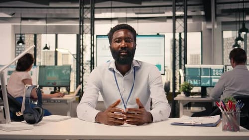 Smiling Man Sitting at Desk in Open Office