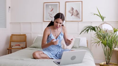Junge Frau sitzt im Schlafzimmer auf dem Bett und führt einen Videoanruf auf dem Laptop