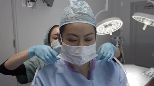 Nurse assists surgeon tying surgical mask in hospital operating room