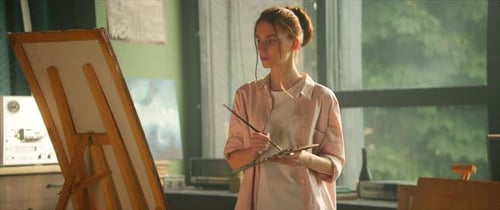 In Art Studio Attractive Young Woman Artist Painting Picture on Canvas Hold Brush and Palette