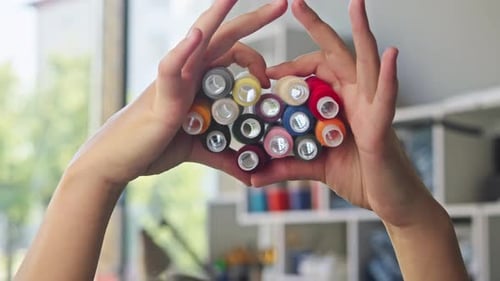 Hands Holding Colorful Thread Spools in Studio