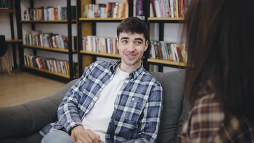 Young Man and Woman Engaged in Friendly Conversation in a Cozy Library Setting During the Afternoon