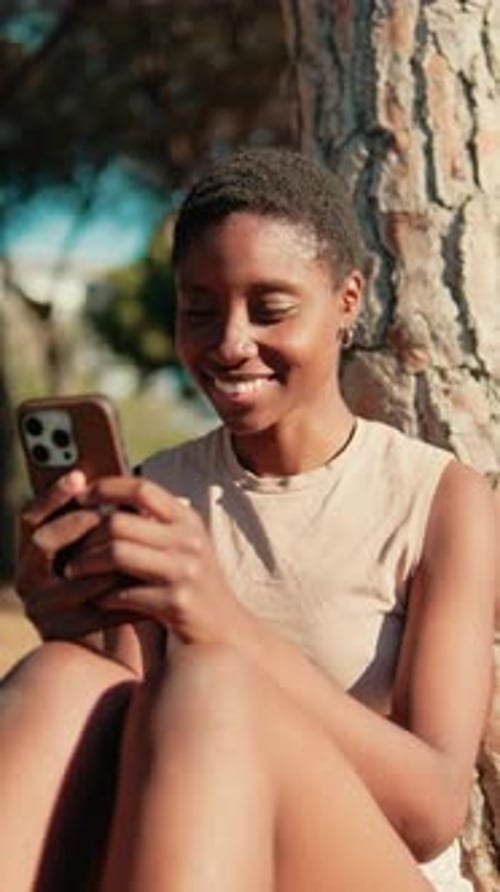 close up video of happy girl sits in the park under a tree with a smartphone in her hands