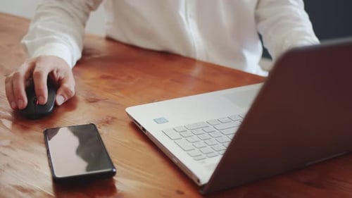 A Young Adult Man in a White Shirt Works on a Laptop with a Wireless Mouse View From Above