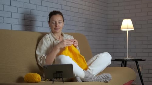 Woman Knitting on Couch While Looking at Tablet