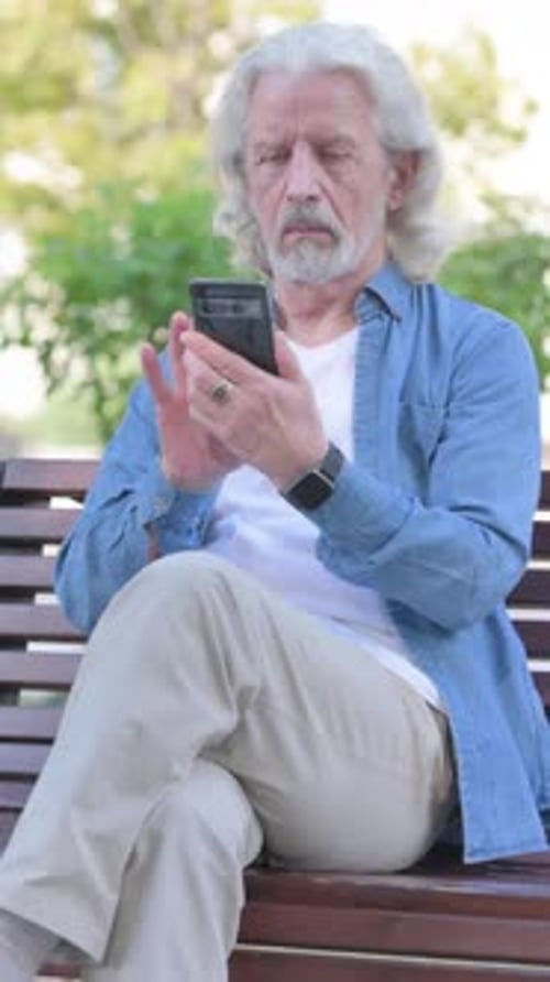 Senior Man Uses Smartphone Device on Park Bench