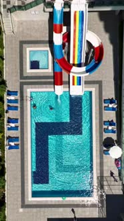 Vertical Video Bright Swimming Pool Area with Kids Sliding Down Water Slides and Splashing Around