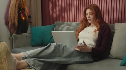 Woman Relaxing on Couch Using Laptop, Drinking Beverage