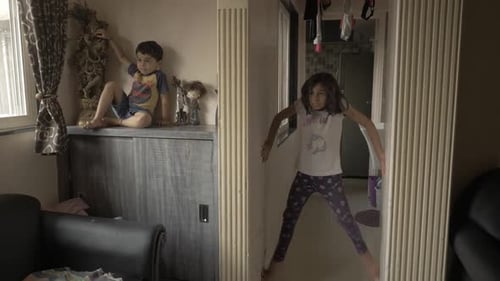 Two little Asian kids playing together separately in one place, sister trying to wall climb and brot