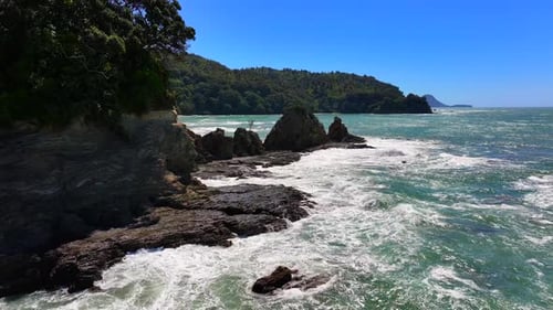 Moody Aerial beech Unspoilt jagged rocky coastline—turquoise waves crash against cliffs, windswept t