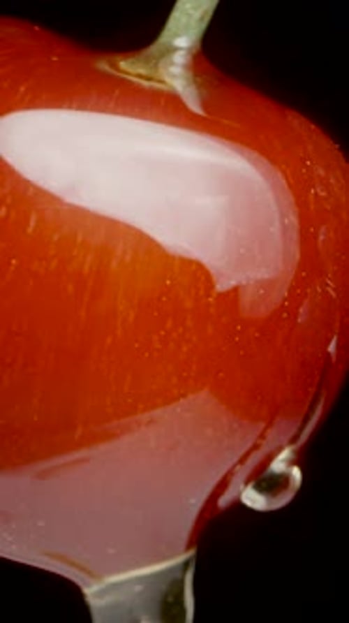 The camera follows the drops rolling onto the cherries, close-up on a black background. Vertical