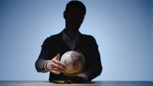 Young Man in the Shade Searching Random Country Turning the Globe and Pointing at Place to Visit