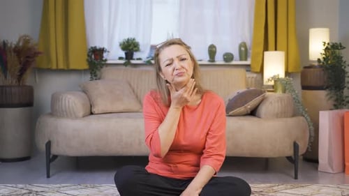 Woman Massaging Sore Throat in Living Room