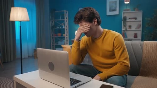 Tired Man Working on Laptop Computer at Home