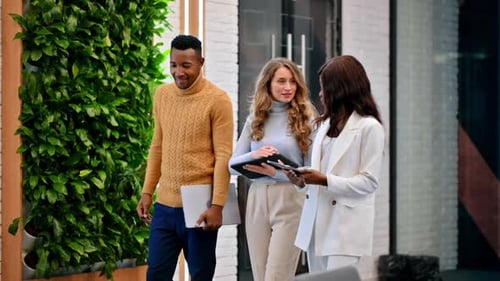 Multiracial group of workers walking in an office and discussing business affairs using tablets. Slo