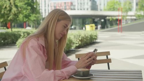 Young Woman Spills Coffee While Browsing Phone At Sunny Outdoor Cafe