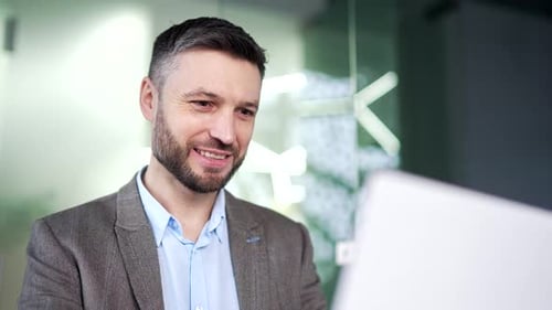 Happy businessman typing on a laptop sitting at a workplace in business office. Handsome