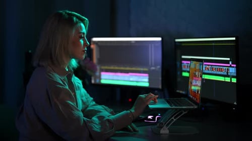 Videofilmerin, weiblich, bearbeitet vom Heimbüro aus mit professionellem Laptop und Desktop mit Ultrawide