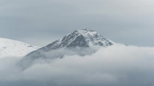 Timelapse clouds covering Snow Capped mountain peaks winter cloudy zoom shot