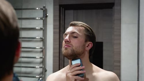 Man Shaves with Electric Razor in Bathroom