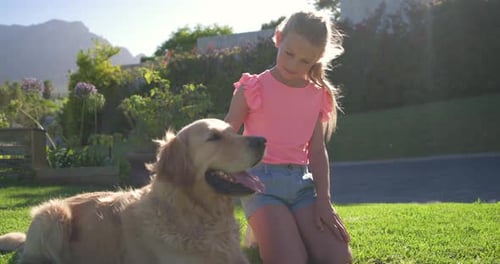 Child girl in pink top noticing panting golden retriever, kneeling and petting to comfort in yard