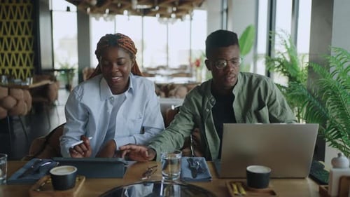 Diverse Team of Two Black Businesspeople Discussing Project Plans in a Cozy Cafe Setting