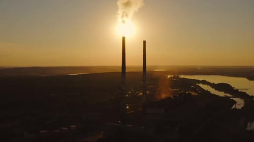 Factory pollutes the atmosphere with harmful emissions. Silhouette of industrial plant among nature.