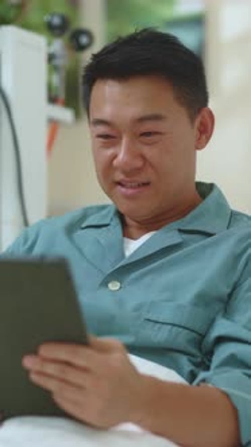 A Man Enjoys Relaxing While Using a Tablet Comfortably in His Bed for Leisure Time