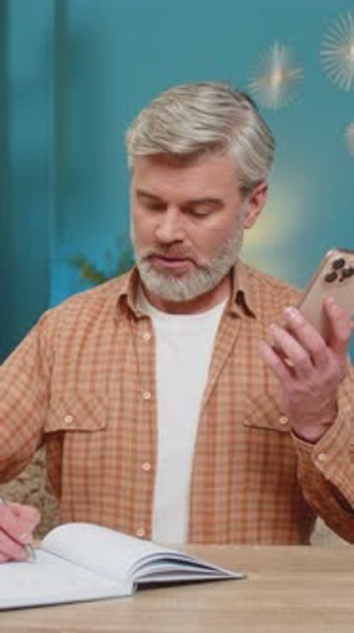 Man at Desk Using Phone While Writing
