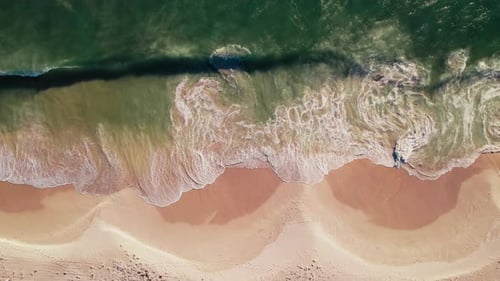 Aerial View of Foamy Waves Crashing on a Sandy Beach