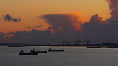 Aerial drone view of multiple oil tankers anchored near an industrial port at sunset with cranes and