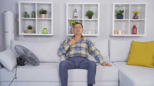 The old man cools down with a fan because of the air temperature.