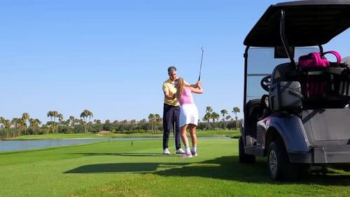 Golf instructor assisting woman practicing swing on golf course
