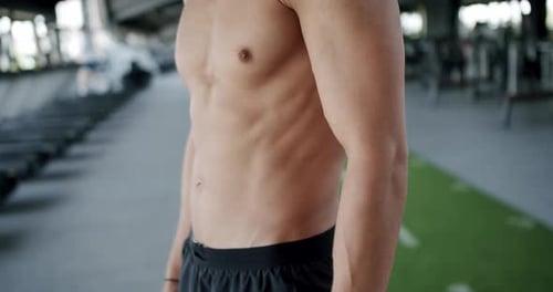 Fit Male Athlete Showing Torso in Gym with Equipment in Background