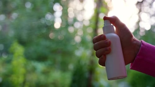 Hand Sprays White Bottle in Forest Setting